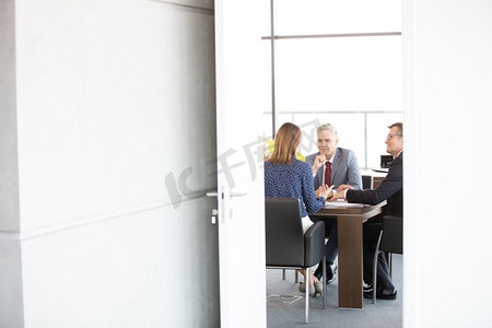 商人和女商人在董事会会议室看到通过打开的门在办公室