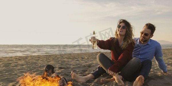 年轻夫妇在炉火边放松，喝啤酒或瓶子里的饮料。