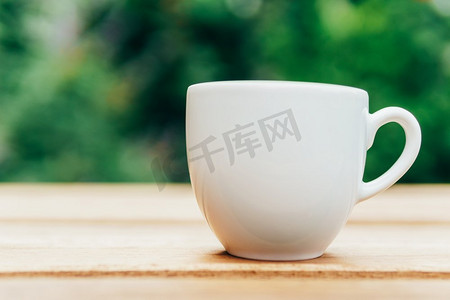 白杯子摄影照片_绿色花园木桌上的白咖啡杯