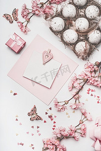 漂亮的粉色复活节贺卡，用鲜花装饰，心形，彩蛋装在纸箱里，白色书桌背景，俯视，平放。