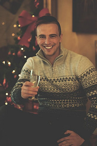 年轻人年轻人聚会摄影照片_年轻人的肖像，拿着香槟酒杯在家里庆祝圣诞节和新年。年轻人在派对上拿着香槟酒杯