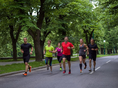 朋友跑步摄影照片_参加晨练的跑步者队。一群健康的人在城市公园慢跑，跑步者团队在晨练