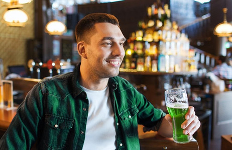色绿摄影照片_人，休闲和圣帕特里克节的概念-在酒吧或酒吧喝绿啤酒的快乐年轻人。在酒吧或酒吧喝绿啤酒的男人