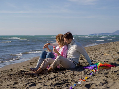 一对年轻的情侣在秋天的海滩上玩得很开心，还在做肥皂泡。一对年轻夫妇在海滩享受着共同的时光