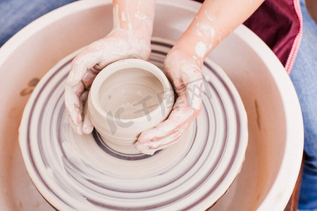 S儿童陶艺工艺品。在陶工的轮子上用白色粘土制作陶器的女孩的手。S儿童陶艺手工艺品