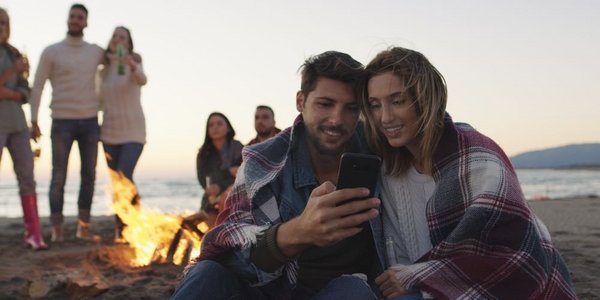 一对情侣在海滩派对上用手机和朋友喝着啤酒玩得开心