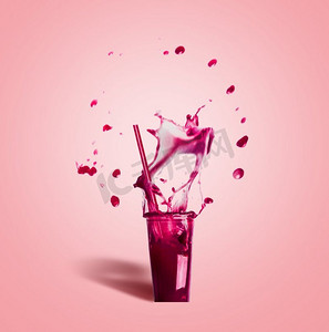 夏天饮料吸管摄影照片_带有吸管和紫色喷洒的夏季饮料的玻璃杯：粉红色背景上的奶昔或果汁，正视