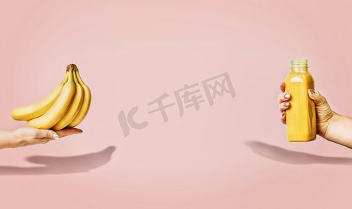 食品模板摄影照片_夏季食品和饮料背景，女性手中拿着香蕉和黄色饮料瓶，采用粉色背景、正视图、横幅或模板。