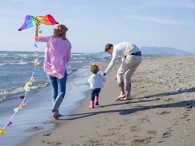 在秋天摄影照片_有小女儿的家庭休息和有乐趣与风筝在海滩在秋天白天。秋日观鸟的幸福家庭