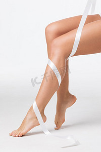 完美妇女的腿特写镜头与白色丝带在白色背景。’完美的女人的腿与白色丝带’