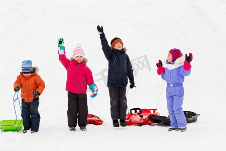 挥舞江湖摄影照片_童年，雪橇和季节概念—一群快乐的小孩子与雪橇在冬天挥舞着手。快乐的孩子与雪橇挥舞的手在冬天