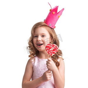 美丽的小糖果公主，戴着王冠，手持大粉色心形棒棒糖，面带微笑。戴皇冠的女孩抱着心形棒棒糖