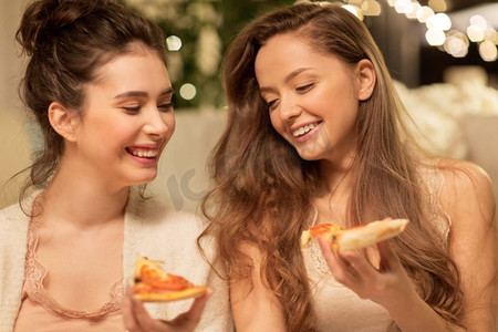 Hygge，食物和睡衣派对概念-快乐的女性朋友或十几岁的女孩在家吃披萨。快乐的女性朋友在家吃披萨