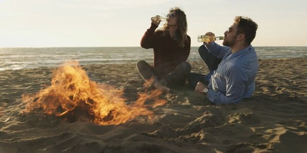 火焰摄影照片_年轻夫妇在炉火边放松，喝啤酒或瓶子里的饮料。