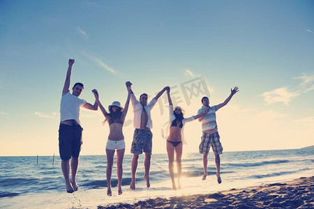 欢乐假期摄影照片_夕阳西下，欢乐青年朋友团在沙滩上跳跃奔跑，尽情玩乐庆祝