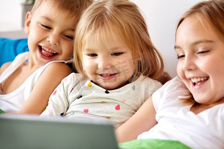 童年、科技和家庭概念-快乐的小孩子在家里的床上玩平板电脑。快乐的小孩子在家里的床上躺着平板电脑