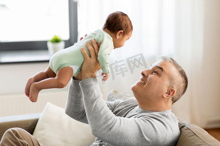 家庭，父亲和人的概念—快乐的父亲与小男婴坐在沙发上在家里。快乐的父亲与小男孩在家里