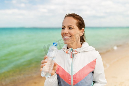 健身、运动和健康的生活方式理念--女性在海滩上运动后喝水。一名女子在海滩上运动后喝水