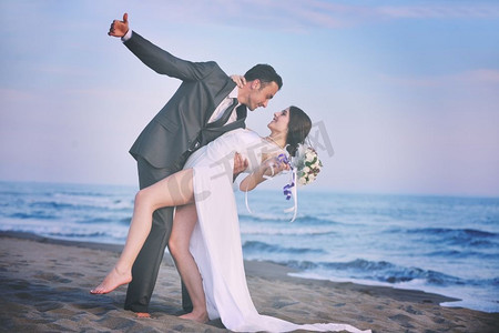 幸福刚刚结婚的年轻夫妇在美丽的日落海滩庆祝和玩乐