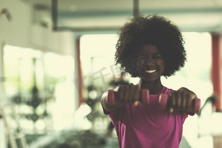 快乐健康的非裔美国女性在CrossFit健身房用哑铃减肥。一名女子戴着哑铃在CrossFit健身房锻炼