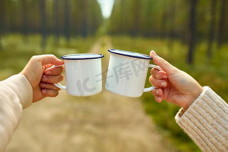 采摘季节，休闲与人的概念--森林中男女手碰白色铁皮茶杯。森林里的一对碰杯的白茶杯