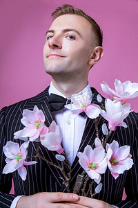 自信的新郎手持人造花站在粉色背景下的肖像