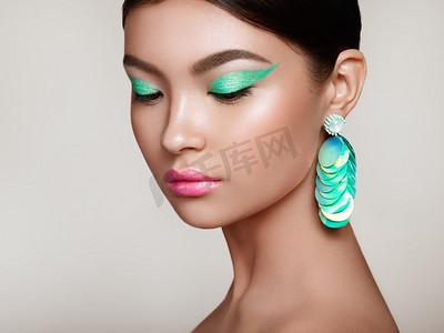 美丽的韩国女人与大绿松石耳环。完美的化妆和优雅的发型。绿松石化妆箭头和粉红色唇膏