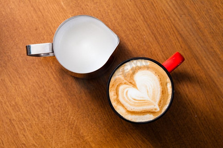 木桌上的一杯红杯拿铁艺术咖啡。顶景木桌上有一杯拿铁艺术卡布奇诺和奶泡罐子