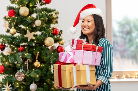 寒假和人们的概念快乐的年轻女子在圣诞树上的礼品盒的背景。带着圣诞礼物的快乐女人