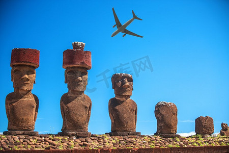 飞机飞过摄影照片_一架旅游飞机飞过复活节岛的雕像。复活节岛