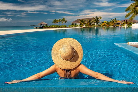 泳游泳摄影照片_马尔代夫海滩泳池边戴帽子的女子。马尔代夫海滩泳池上戴太阳帽的女子
