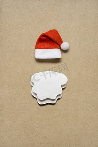 圣诞老人帽子摄影照片_棕色背景下圣诞老人帽子和胡须的创意概念照片。