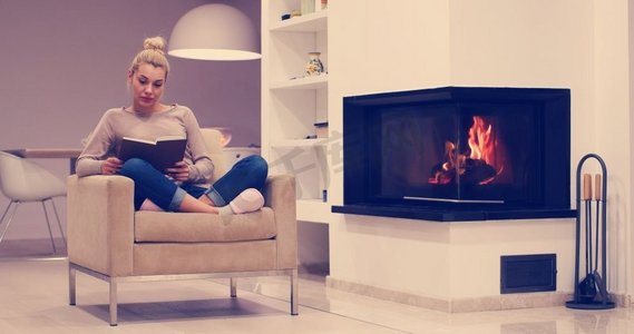 年轻美丽的女人坐在壁炉前在家里在一个寒冷的秋天和读书