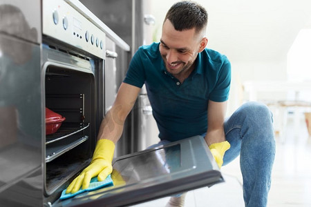 家居和人的概念--男人擦桌子，用布清洗家里厨房的烤箱门。在家里厨房里拿着抹布清洁炉门的男人