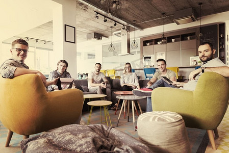 现代办公室里的年轻人群体一边工作着笔记本电脑，一边喝着咖啡，举行团队会议和头脑风暴