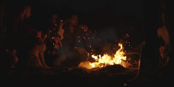 晚上，年轻夫妇和朋友围着篝火坐在海滩上喝啤酒