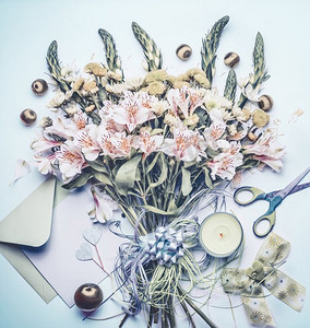 美丽的节日鲜花花束与信封，空白的问候卡，剪刀和蜡烛在粉彩蓝色背景，顶视图，平奠定
