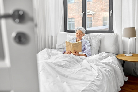 老年、休闲与人的概念--老年妇女在家中卧室的床上读书。老年妇女在家里卧室的床上看书