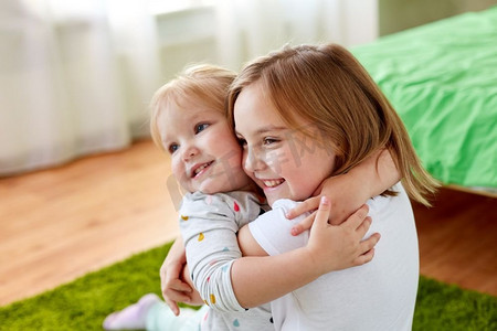 童年，家庭，表情和人的概念-快乐的小女孩或姐妹在家里拥抱。快乐的小女孩或姐妹们在家中拥抱