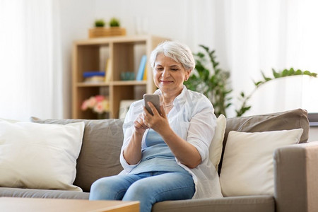 技术，通信和人的概念—快乐的高级妇女与智能手机在家里。快乐的高级妇女与智能手机在家里