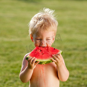 户外学步儿童的肖像。一岁男婴在花园里吃西瓜片的乡间场景。快乐孩子脏兮兮的脸。