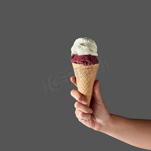 和牛奶冰淇淋,呈球形,装在华夫饼锥中,由灰色背景下的女人手握着