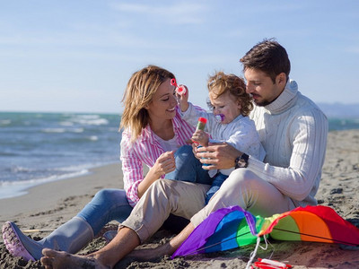 矢矢摄影照片_家庭与小女儿休息和有乐趣使肥皂泡在海滩在秋天。在秋天享受矢量化的年轻家庭