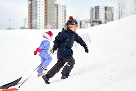 童年，雪橇和季节概念—快乐的小孩子与雪橇爬雪山在冬天。孩子们带着雪橇爬雪山在冬天