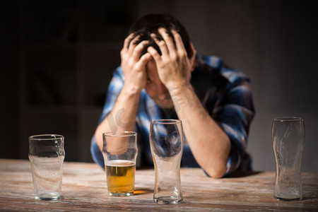 酒精中毒,酒精成瘾和人们的观念-男性酗酒者晚上从玻璃杯中喝啤酒.