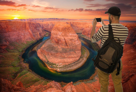 一名男性游客在科罗拉多河著名的马蹄弯拍照。亚利桑那