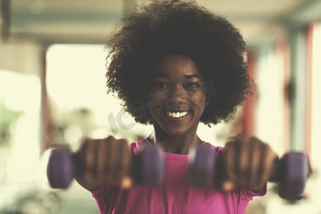 快乐健康的非裔美国女性在CrossFit健身房用哑铃减肥。一名女子戴着哑铃在CrossFit健身房锻炼