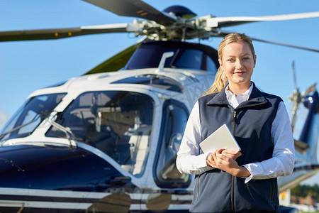 女飞行员手持数字平板电脑站在直升机前的肖像