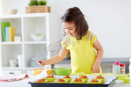 家庭，烹饪，烘焙和人的概念—小女孩在家庭厨房做松饼或纸杯蛋糕面糊。小女孩在家里烤松饼