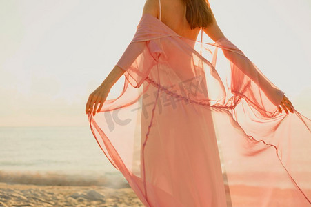 粉红色孕妇摄影照片_户外大气生活方式肖像美丽的孕妇粉红色连衣裙。美好的早晨。海滩上的日出。美容和时尚